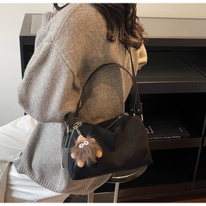 Detail of a black crescent shoulder bag with a cute brown plush monster charm accessory