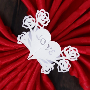 Detail of white laser-cut paper napkin ring with heart and rose pattern showing LOVE text