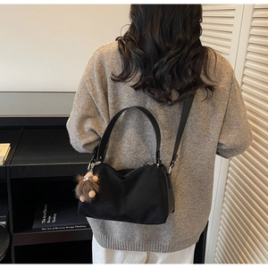 Close-up of a minimalist black crossbody bag featuring a cute brown plush bear charm