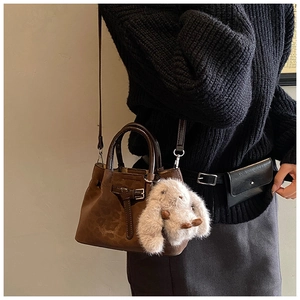 Detail of brown suede bucket bag with leather strap and plush rabbit charm on model