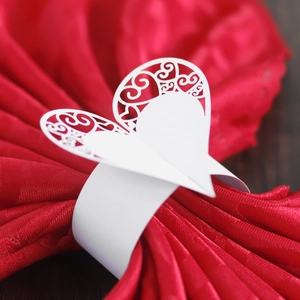 Detail of laser-cut white paper napkin ring with hollow heart pattern on red fabric