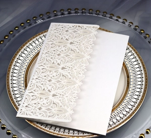 Detail of laser-cut pearl white wedding invitation with intricate floral lace texture
