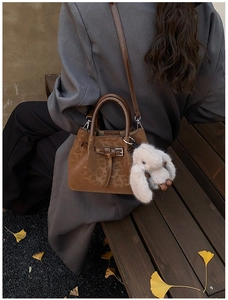 Close-up of a dark brown retro pleated handbag featuring a cute plush bunny charm detail
