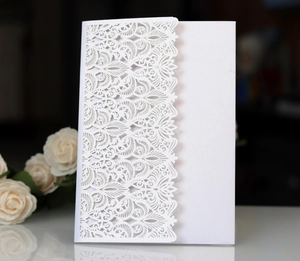 Detail of laser-cut white pearlescent paper invitation with intricate floral lace patterns