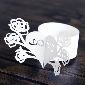 Detailed macro view of laser-cut white paper napkin ring featuring LOVE and rose design