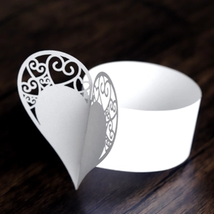 Macro view of white laser-cut heart paper napkin ring on a dark wood background