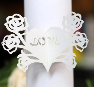 Macro detail of laser-cut white paper napkin ring with heart shape and LOVE text