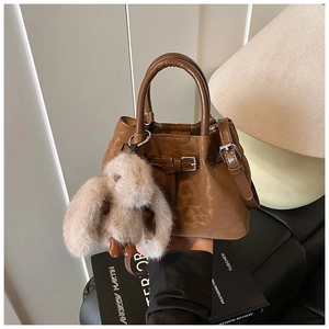 Detail of warm brown leather bucket bag featuring a cute plush bunny charm and strap
