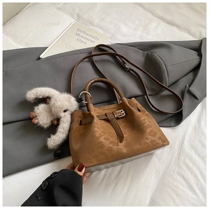 Detail of a brown pleated tote bag with fine buckle design and a plush rabbit pendant