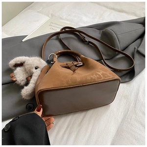 Detail of a brown bucket bag in suede and smooth leather with a plush elephant charm