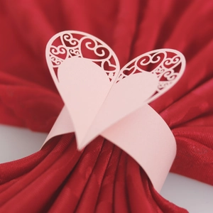 Close-up of pink laser-cut heart paper napkin ring on elegant red fabric decor