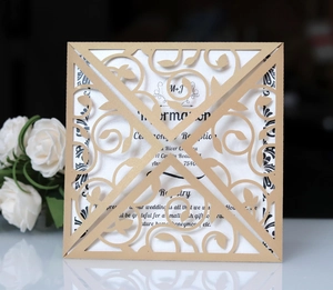 Detail of laser-cut gold wedding invitation with intricate floral patterns and insert card