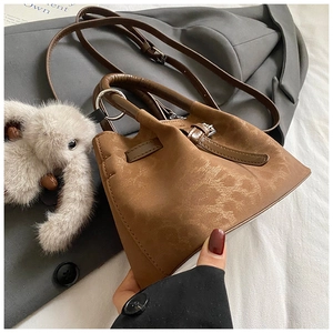 Detail of brown pleated bucket bag with metallic ring handle and white plush charm