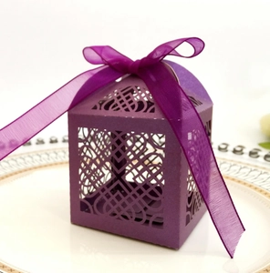 Elegant purple laser-cut wedding favor box with a delicate ribbon bow on white porcelain