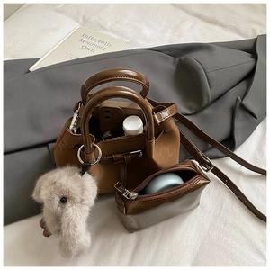 Detail of retro brown bucket bag set with elephant plush charm on a cozy white bedsheet