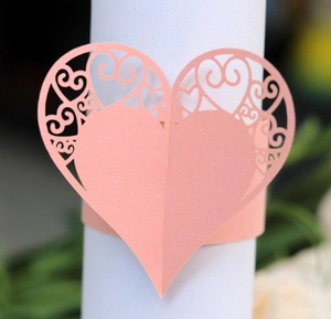 Detail of laser-cut heart paper napkin ring with delicate hollow pattern in peach pink