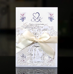 Elegant laser-cut white wedding invitation with floral patterns and cream satin bow