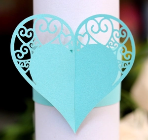Detail of laser-cut heart paper napkin ring with cyan hollow scroll patterns for weddings