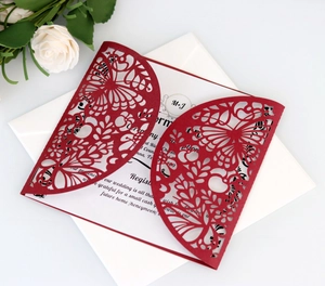 Close-up of laser-cut burgundy wedding invitation with elegant butterfly and floral patterns