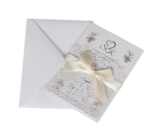 Detail of laser-cut floral lace wedding invitation with a silk bow and white envelope