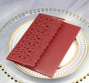 Macro shot of dark red laser-cut wedding invitation with intricate lace vine patterns