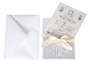 Detailed view of white laser-cut wedding invitation set with ribbon bow and envelope