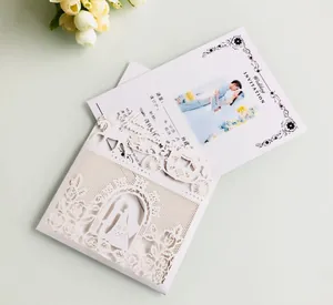 Close-up of laser-cut white wedding invitation with intricate carriage and rose patterns