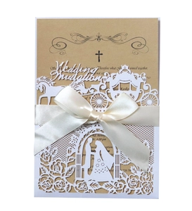 Detail of laser-cut white wedding invitation with pumpkin carriage and cream ribbon