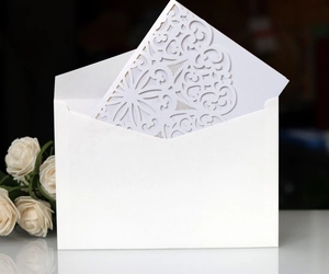 Detail of white laser-cut floral wedding invitation card with matching envelope