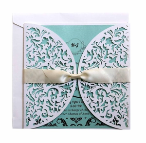 Detail of laser-cut floral wedding invitation with teal inner card and cream ribbon bow