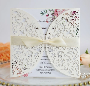 Close-up of laser-cut ivory wedding invitation with silk ribbon and floral insert