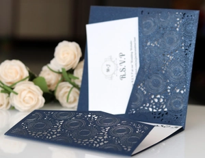 Close-up of laser-cut navy blue wedding invitation with RSVP card and white rose detail