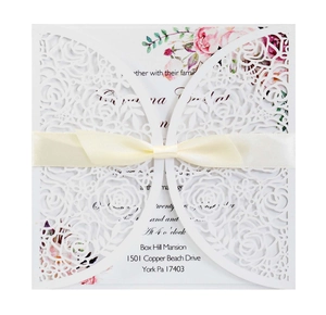 Macro view of laser-cut rose invitation card with elegant cream satin ribbon bow