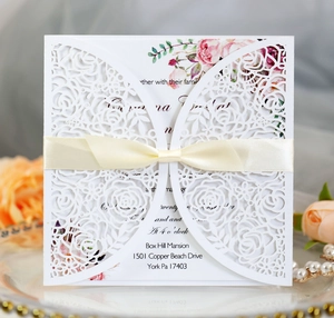 Elegant laser-cut floral wedding invitation with cream satin bow and floral inner card