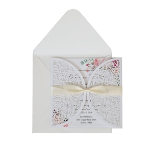 Close-up of white laser-cut rose wedding invitation set with cream satin ribbon
