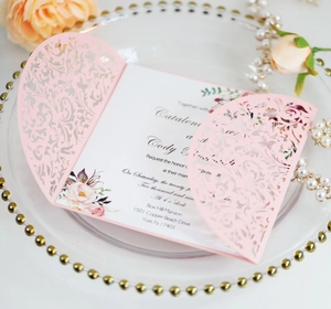Detail of pink laser-cut wedding invitation with elegant floral insert on gold tray