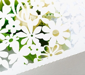 Detail of laser-cut white cardstock showing intricate hollow floral and leaf patterns