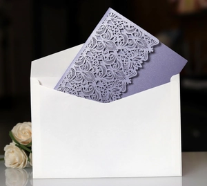 Macro shot of purple laser-cut wedding invitation with lace patterns and white envelope