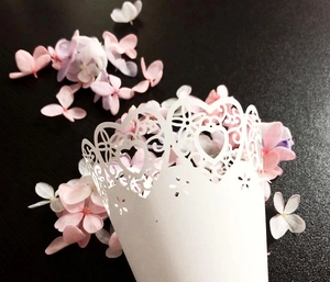 Macro shot of white laser-cut wedding cone with heart hollow pattern and flower petals