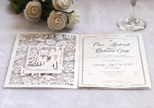 Detail of laser-cut ivory wedding invitation with floral borders and couple silhouette
