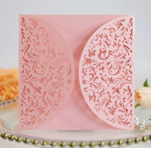 Close-up of pink laser-cut wedding invitation with intricate floral lace on a glass tray