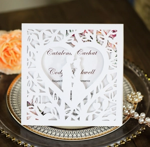 Elegant white laser-cut wedding invitation featuring a heart-shaped tree and couple silhouette