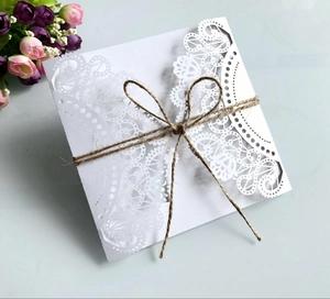 Detail of laser-cut white wedding invitation card with twine bow and floral accents