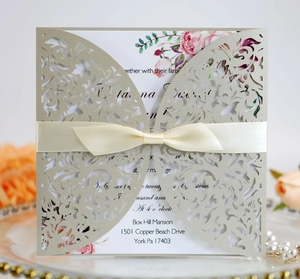 Detail of laser-cut champagne gold wedding invitation with satin bow and floral insert