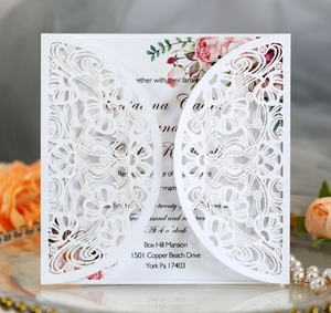 Detail of laser-cut white wedding invitation envelope with floral insert card on mirror