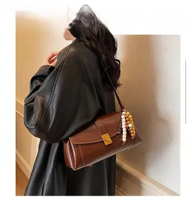 Detail of brown leather pillow bag with gold lock and wooden bead pendant accessory