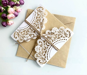 Detail of laser-cut lace wedding card with kraft envelope and rustic twine on floral background