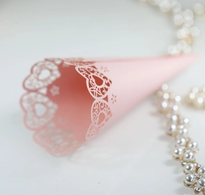 Detailed view of pink laser-cut paper cone with delicate heart filigree for wedding favors