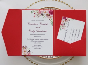 Detail of red floral wedding invitation suite with RSVP card on decorative gold plate