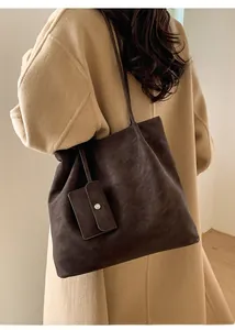 Detail view of brown matte leather tote bag with small card holder charm on shoulder